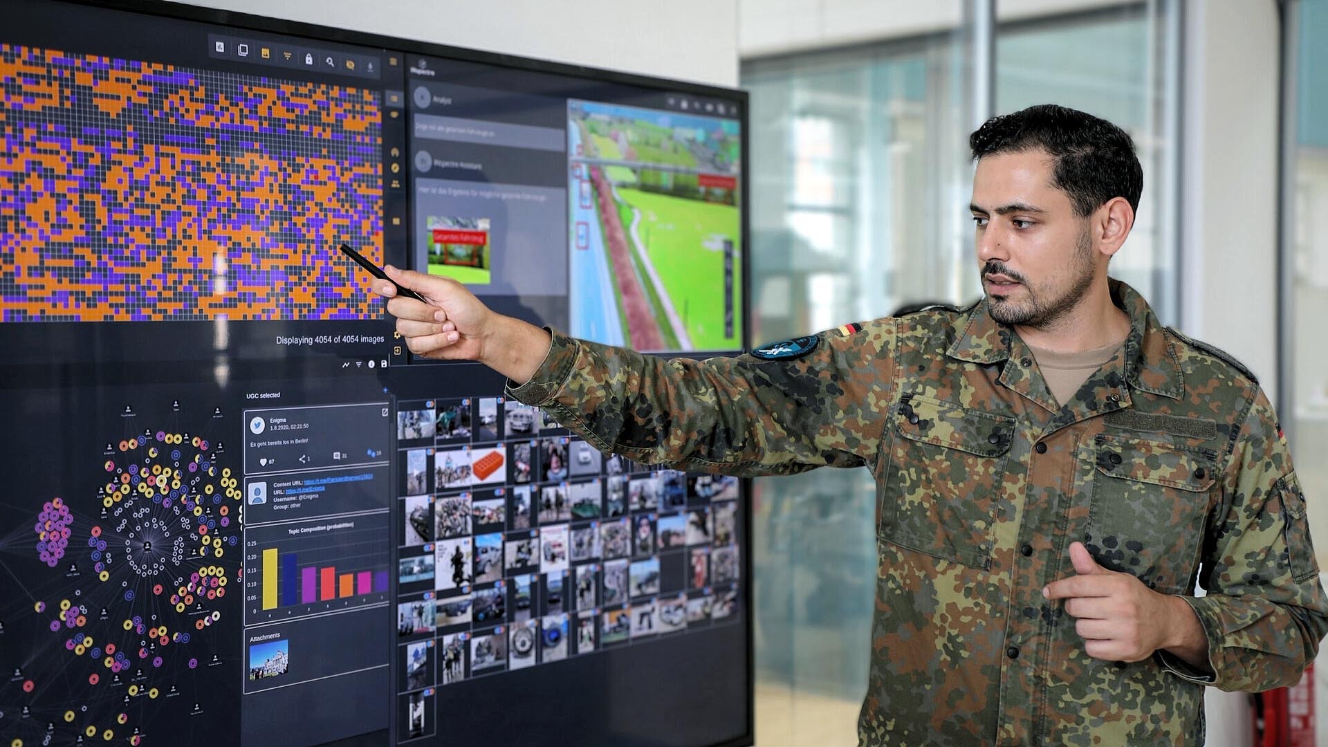 Soldat zeigt mit Stift auf Datenvisualisierung am Monitor