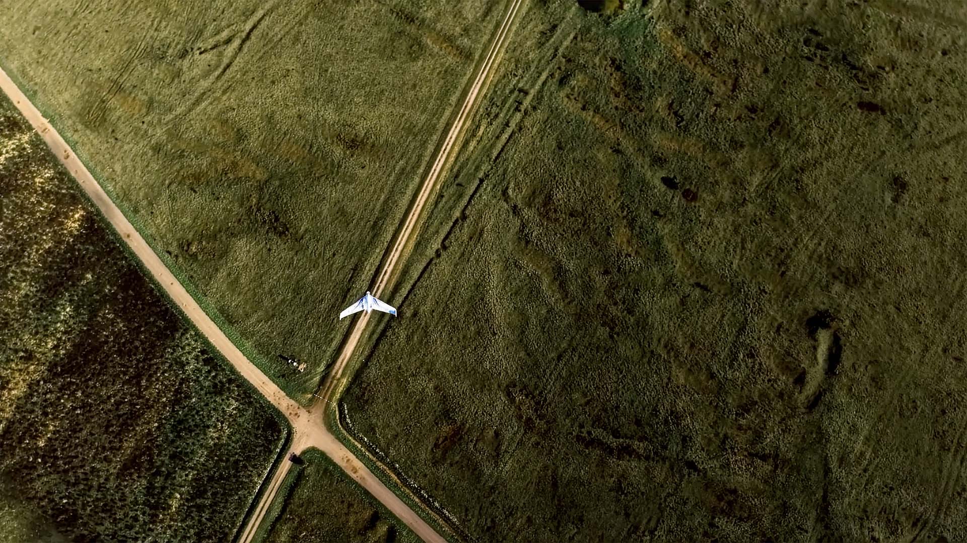 Drohne fliegt über Feld entlang Kreuzung aus unbefestigten Wegen