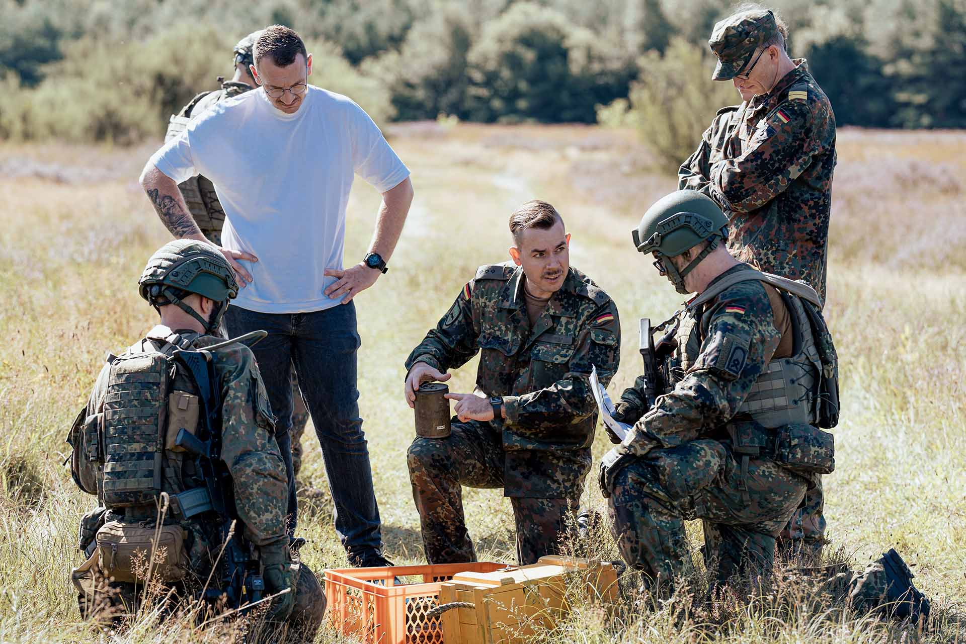 Mehrere Soldaten und Zivilperson besprechen Ausrüstung im freien Gelände