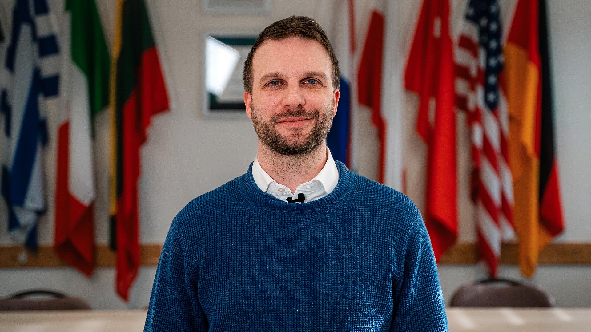 Jan Phillip Krahn, Produktmanager Intrapreneurship steht vor Flaggen und blickt in die Kamera