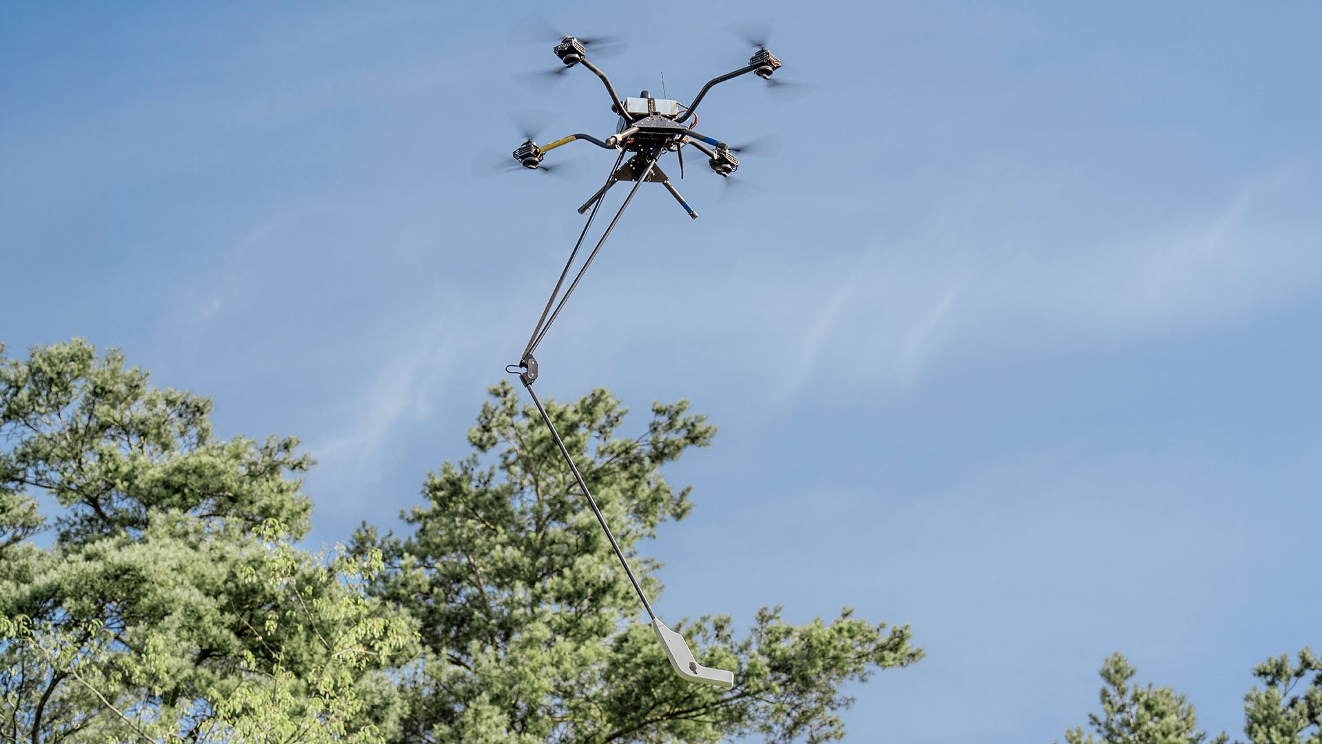 Mehrrotor-Drohne mit Sensorstange fliegt über Bäumen
