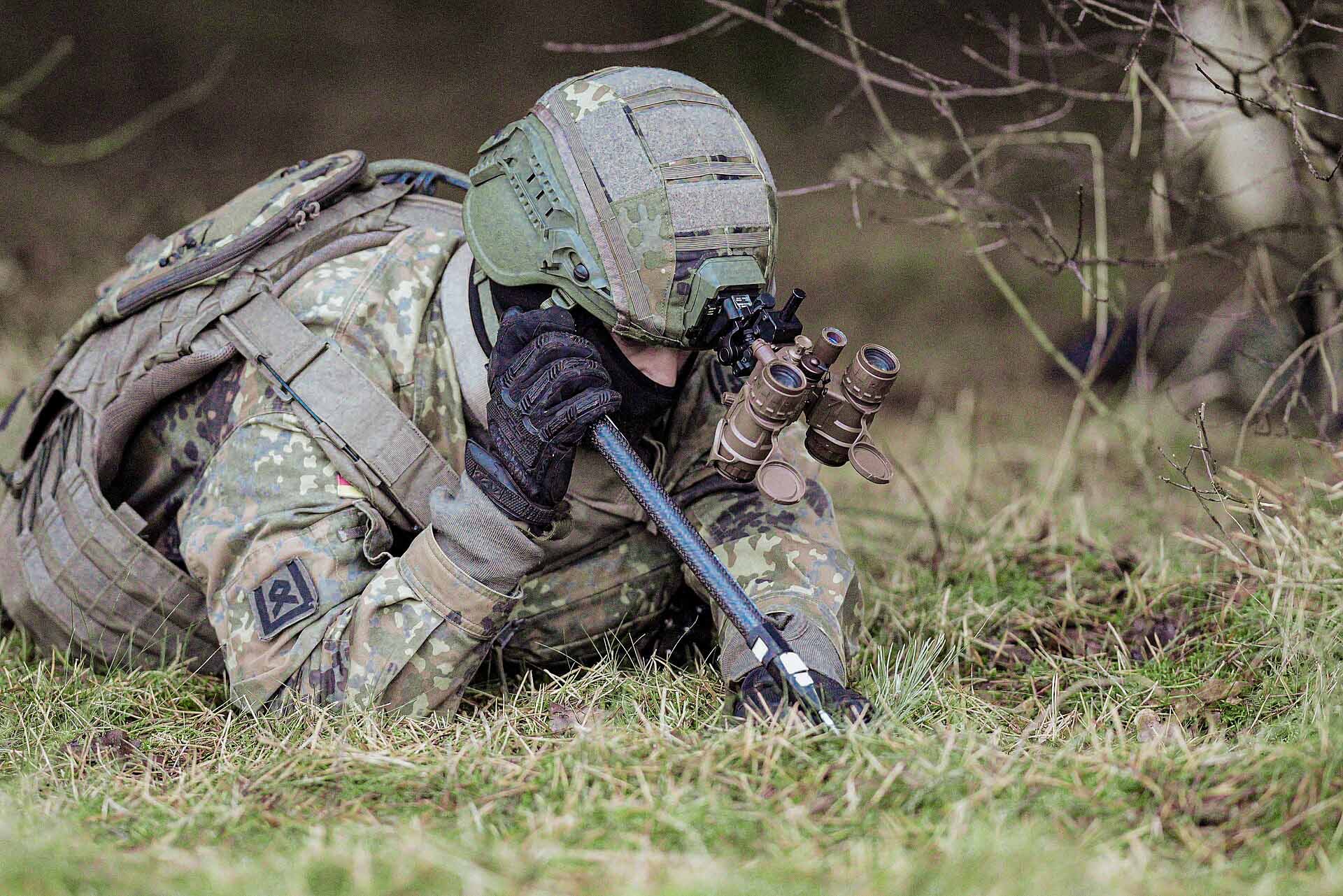 Soldat liegt getarnt im Gras mit Beobachtungsgerät