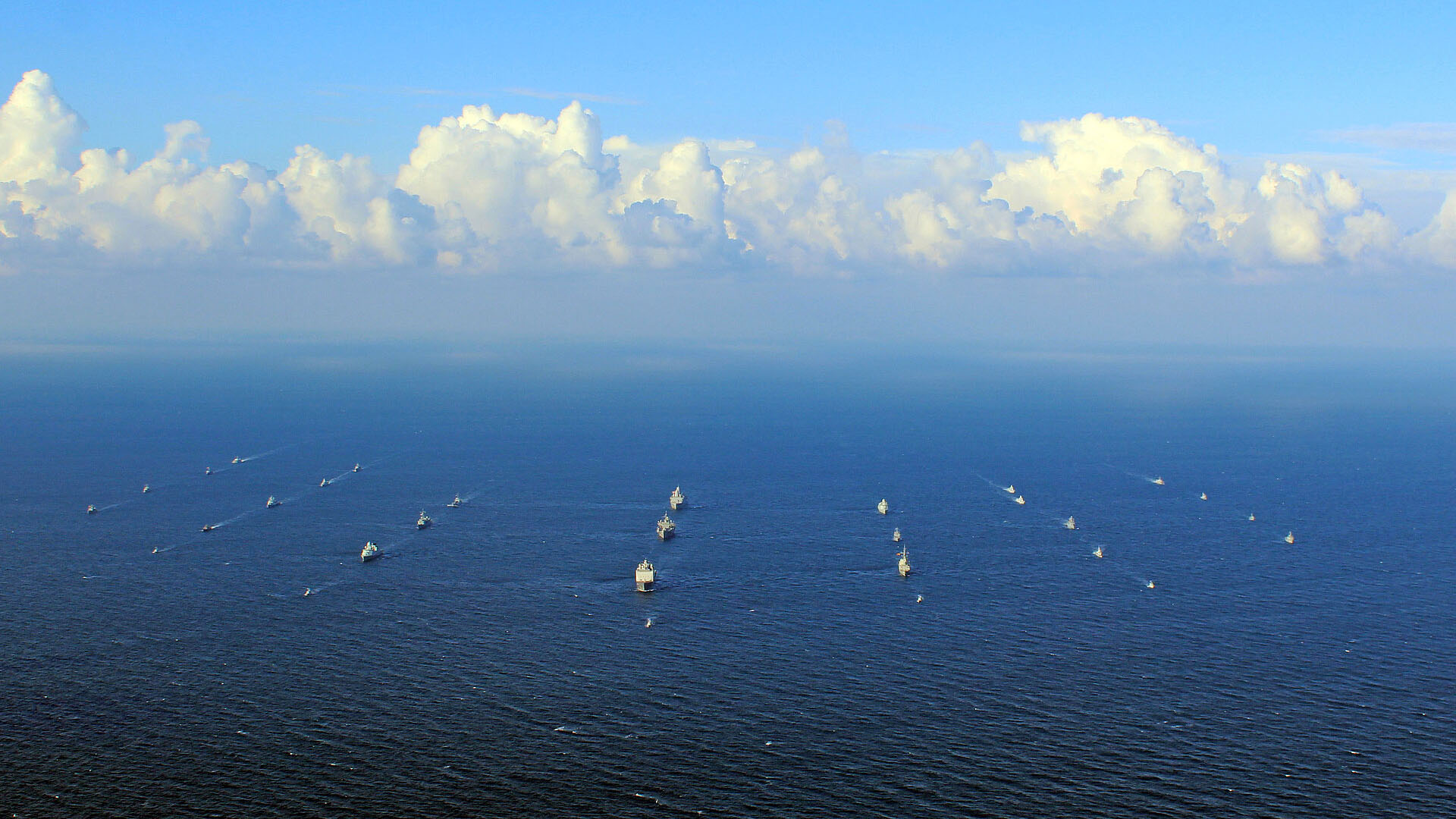 Mehrere Schiffe fahren in Formation auf offenem Meer unter Wolken