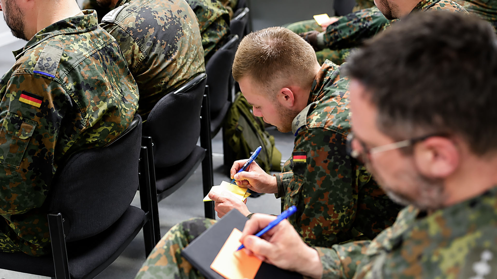 Soldaten in Uniform machen Notizen während Veranstaltung im Sitzen