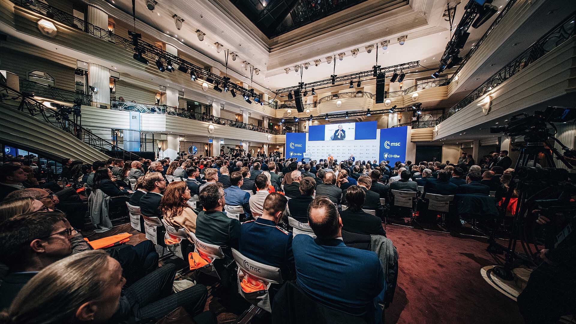 Publikum sitzt in Konferenzsaal vor Bühne mit Paneldiskussion