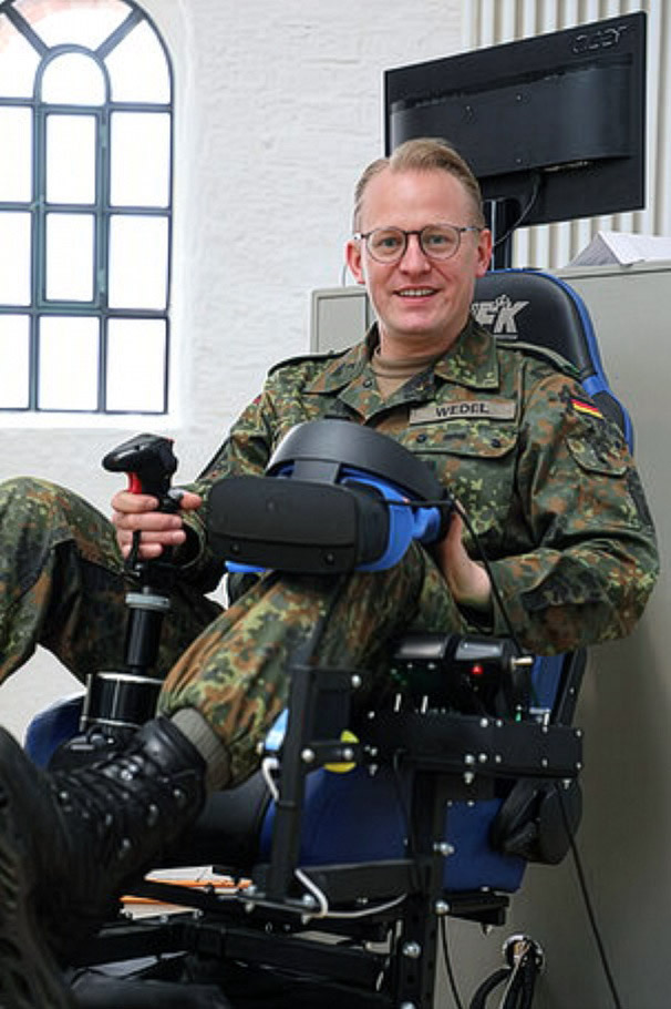 Oberleutnant Hubertus sitzt auf Trainingsgerät und hält Virtual-Reality-Brille