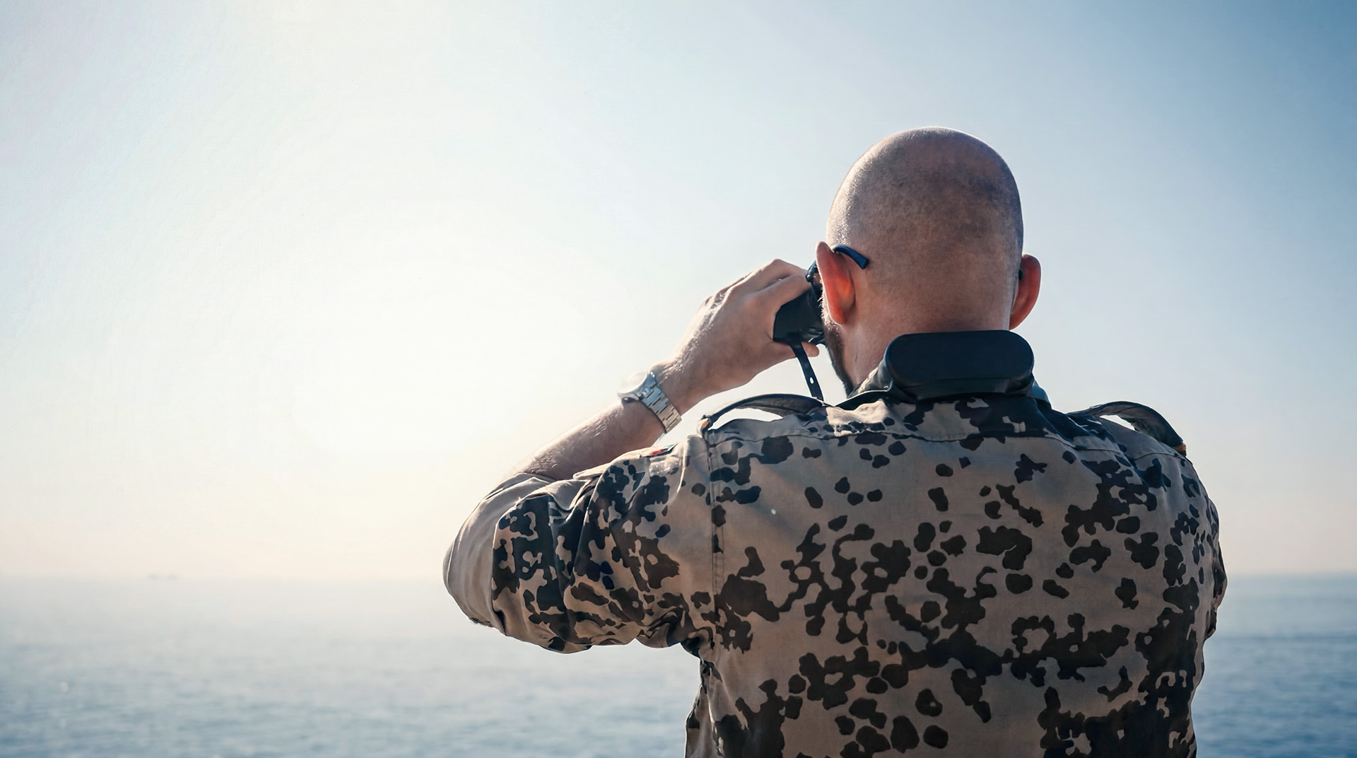 Person blickt mit Fernglas auf See aus erhöhter Position