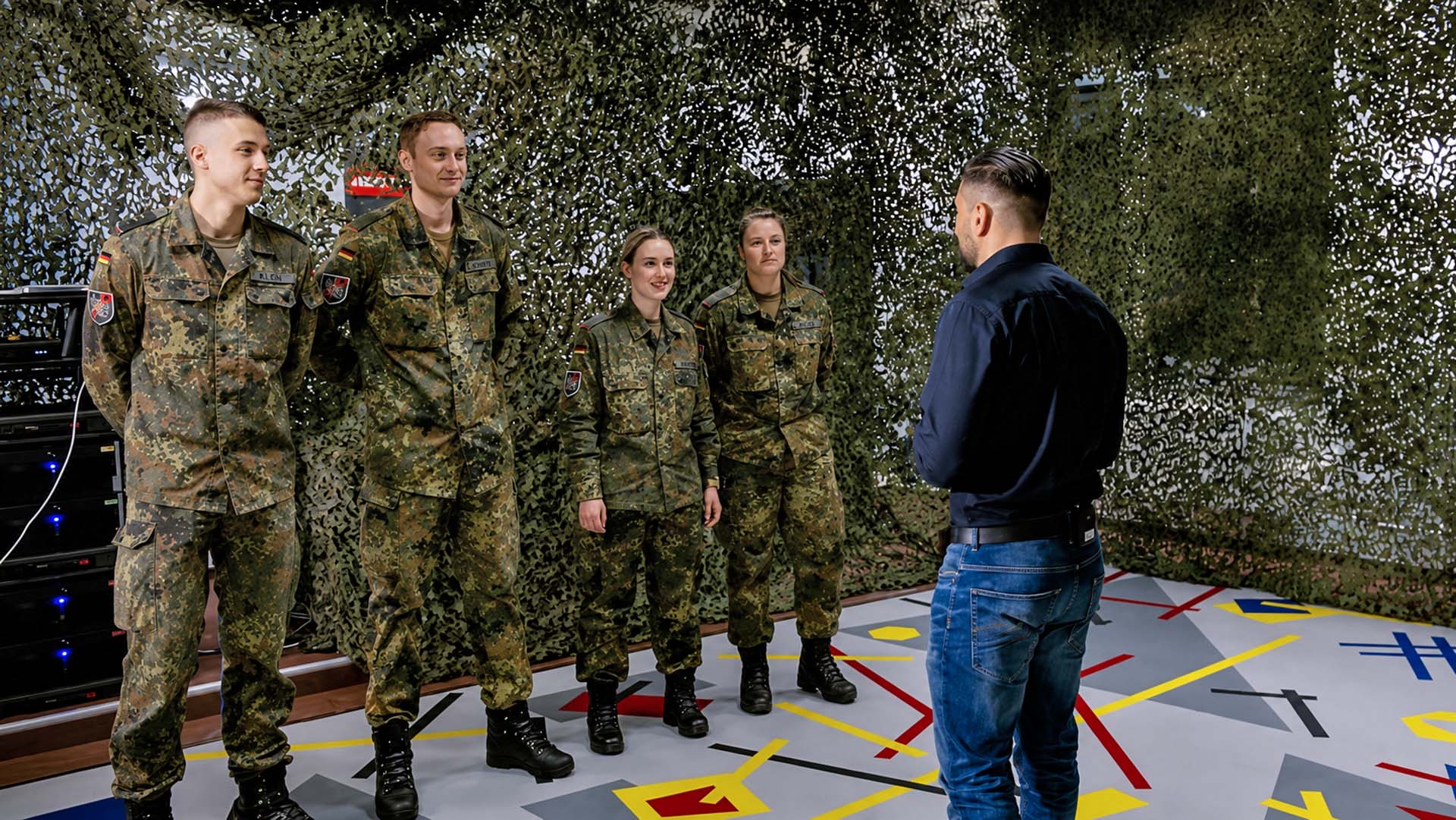 Vier Soldaten stehen in Reihe und hören Anleitung im Trainingsraum