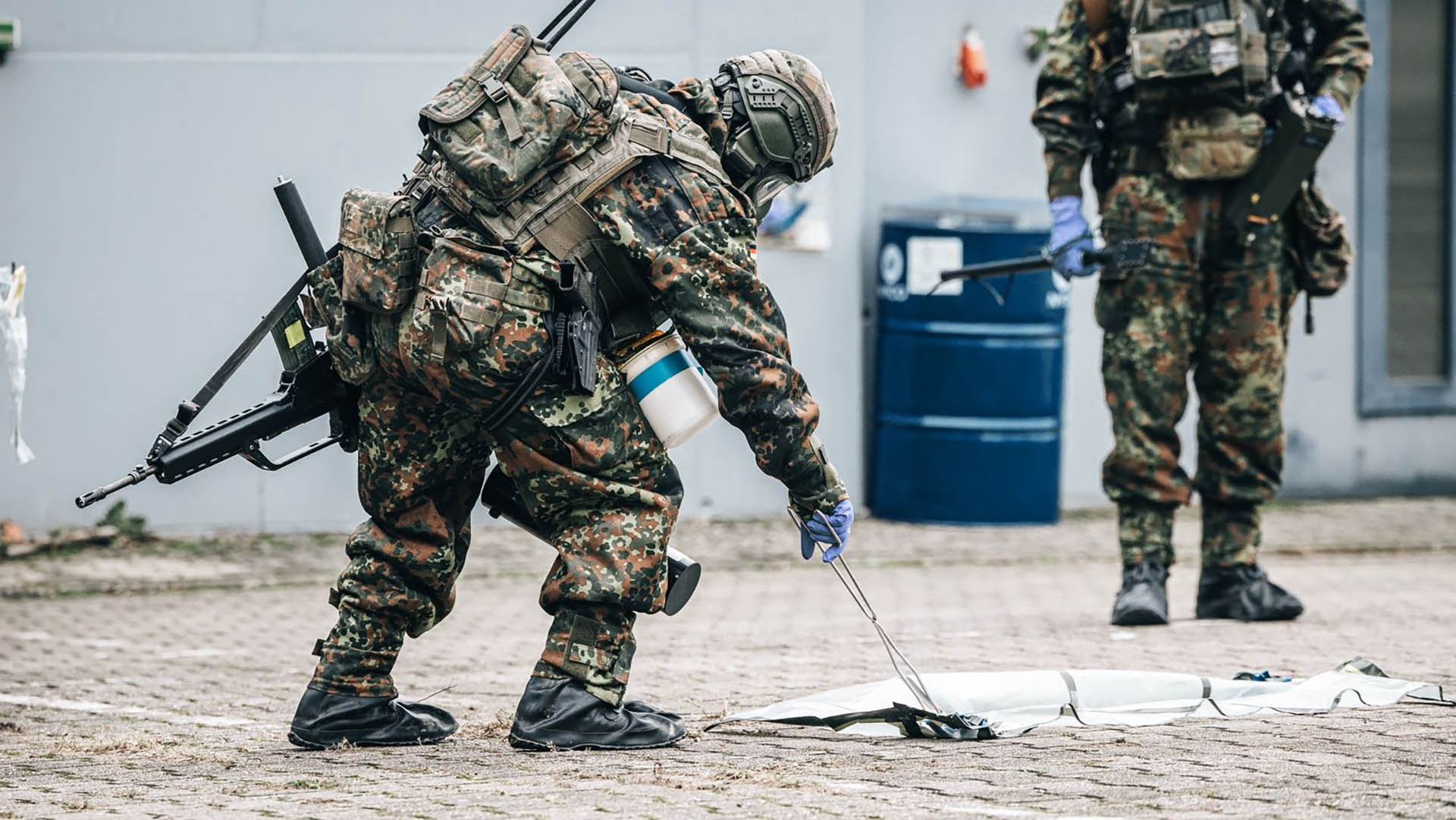 Soldat untersucht Boden mit Messsonde zwischen Gebäuden