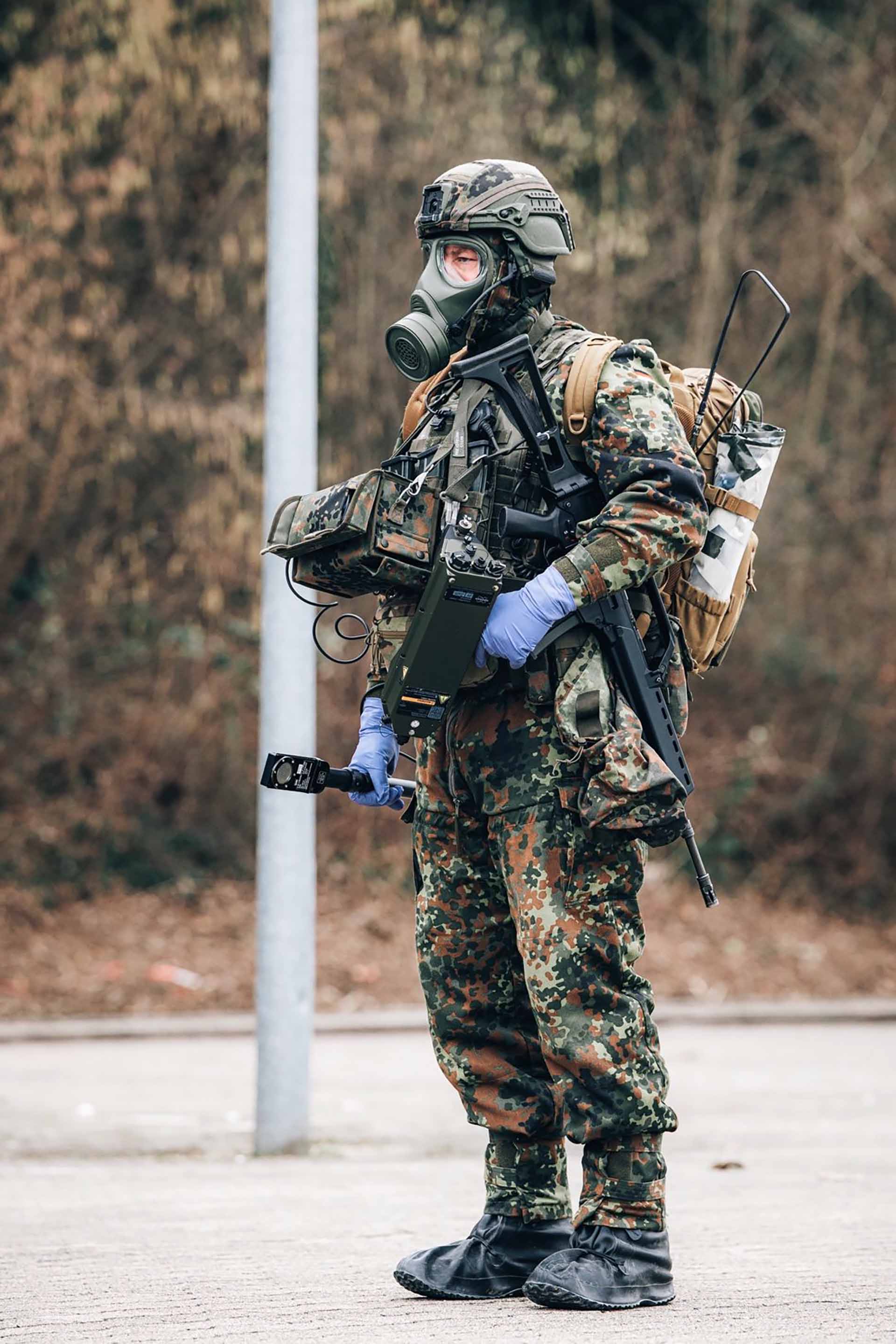 Soldat in Schutzmaske trägt Messgerät im Außenbereich