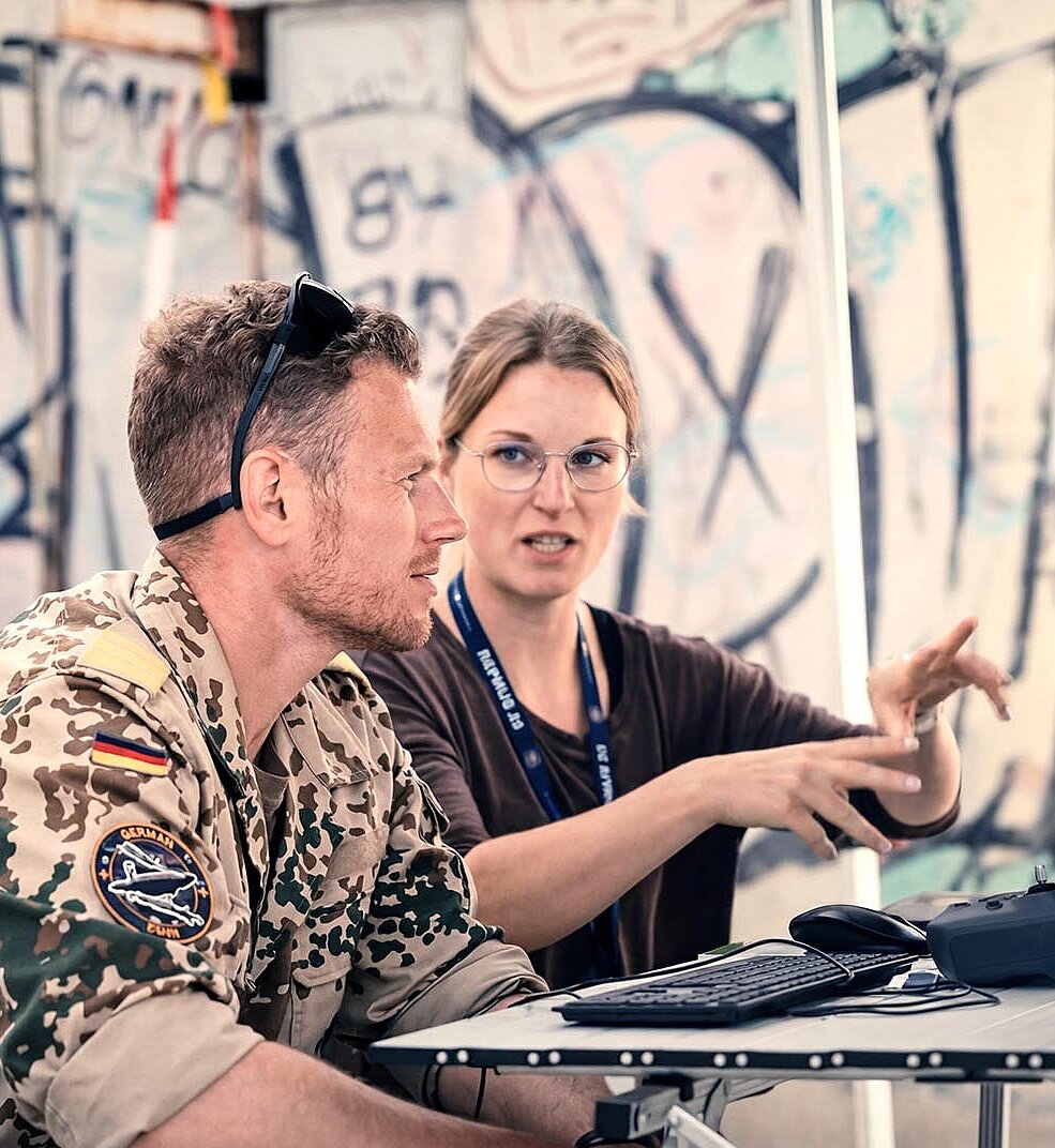 Zwei Personen arbeiten gemeinsam an Computerarbeitsplatz im Außenbereich