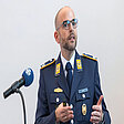Major Michael Frick spricht an Rednerpult in Innenraum mit Mikrofon