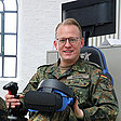 Oberleutnant Hubertus sitzt auf Trainingsgerät und hält Virtual-Reality-Brille