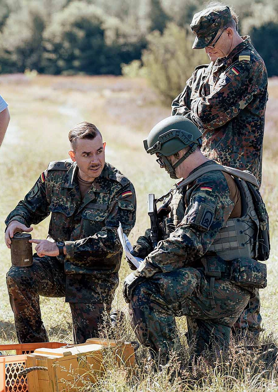 Mehrere Soldaten und Zivilperson besprechen Ausrüstung im freien Gelände