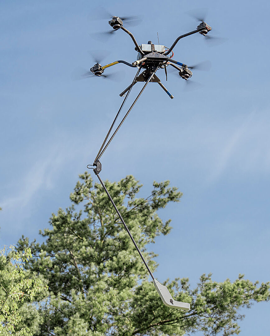 Mehrrotor-Drohne mit Sensorstange fliegt über Bäumen