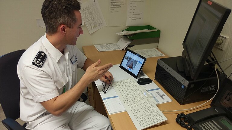 A doctor sits at his desk and talks to a patient via video telephony on his iPad