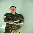 Hauptmann Sandro steht in Uniform lächelnd vor neutralem Hintergrund