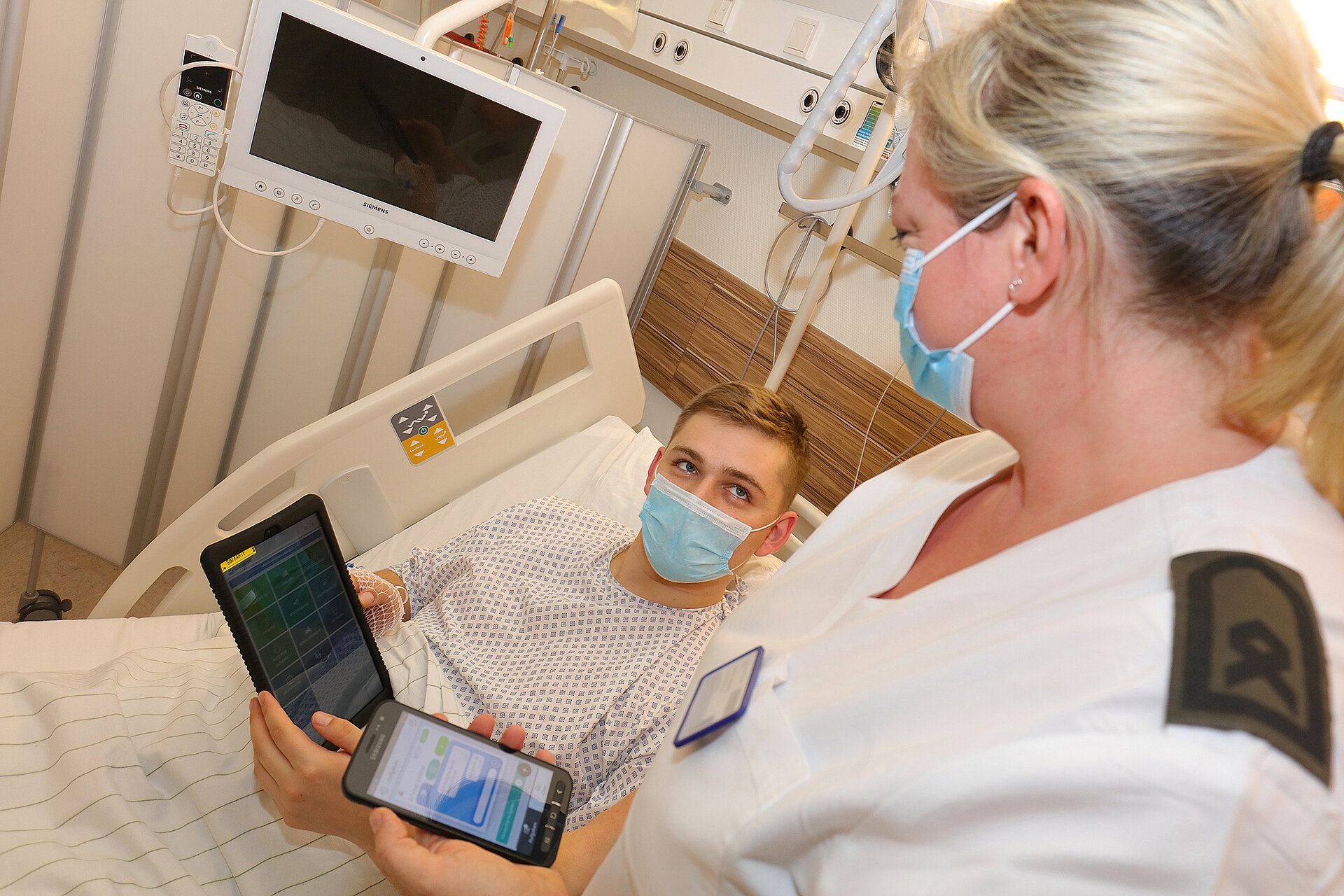 Patient hält Tablet mit der Pflegeapp und Pflegerin erklärt ihm diese.