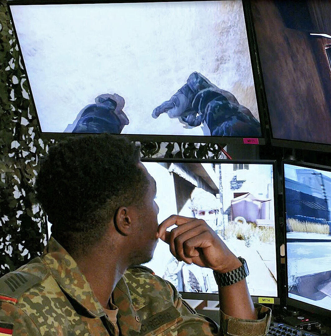 Soldat betrachtet mehrere Monitore mit militärischer Simulationsansicht