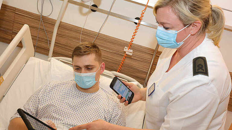 Ein Patient und eine Ärztin am Krankenhausbett mit einem Tablet und einem Smartphone