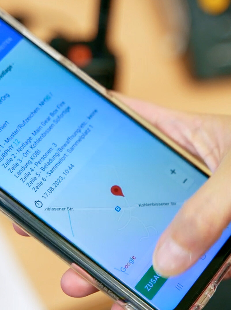 Hand hält Smartphone mit Einsatzmeldung und Kartenansicht