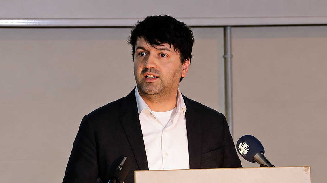 Sven Weizenegger spricht am Rednerpult vor Publikum und Mikrofonen