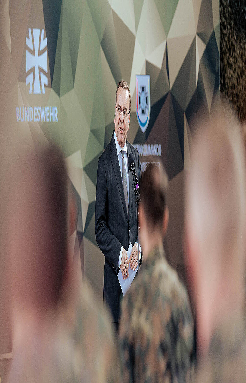 Person spricht am Mikrofon vor Bundeswehr-Logo und Publikum