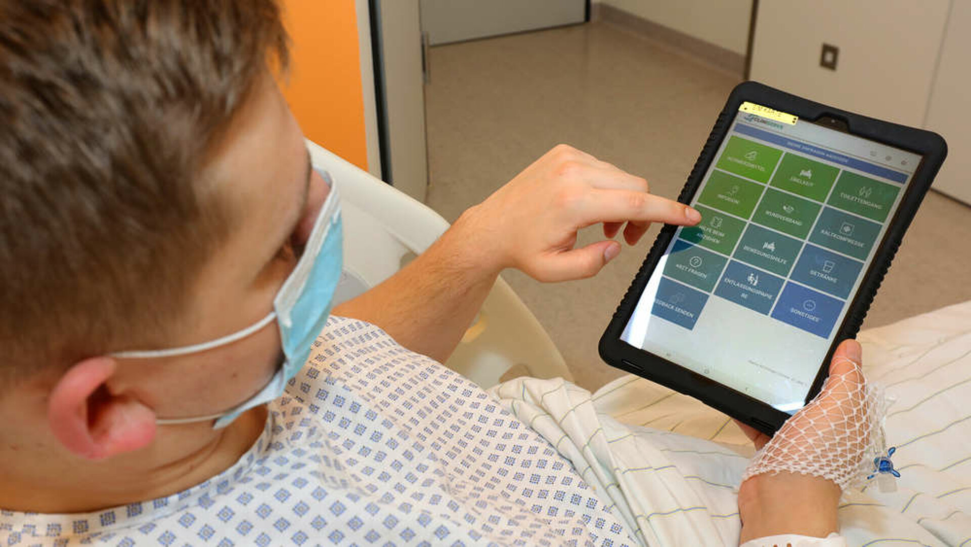 Ein Patient im Krankenhausbett tippt auf einem iPad.