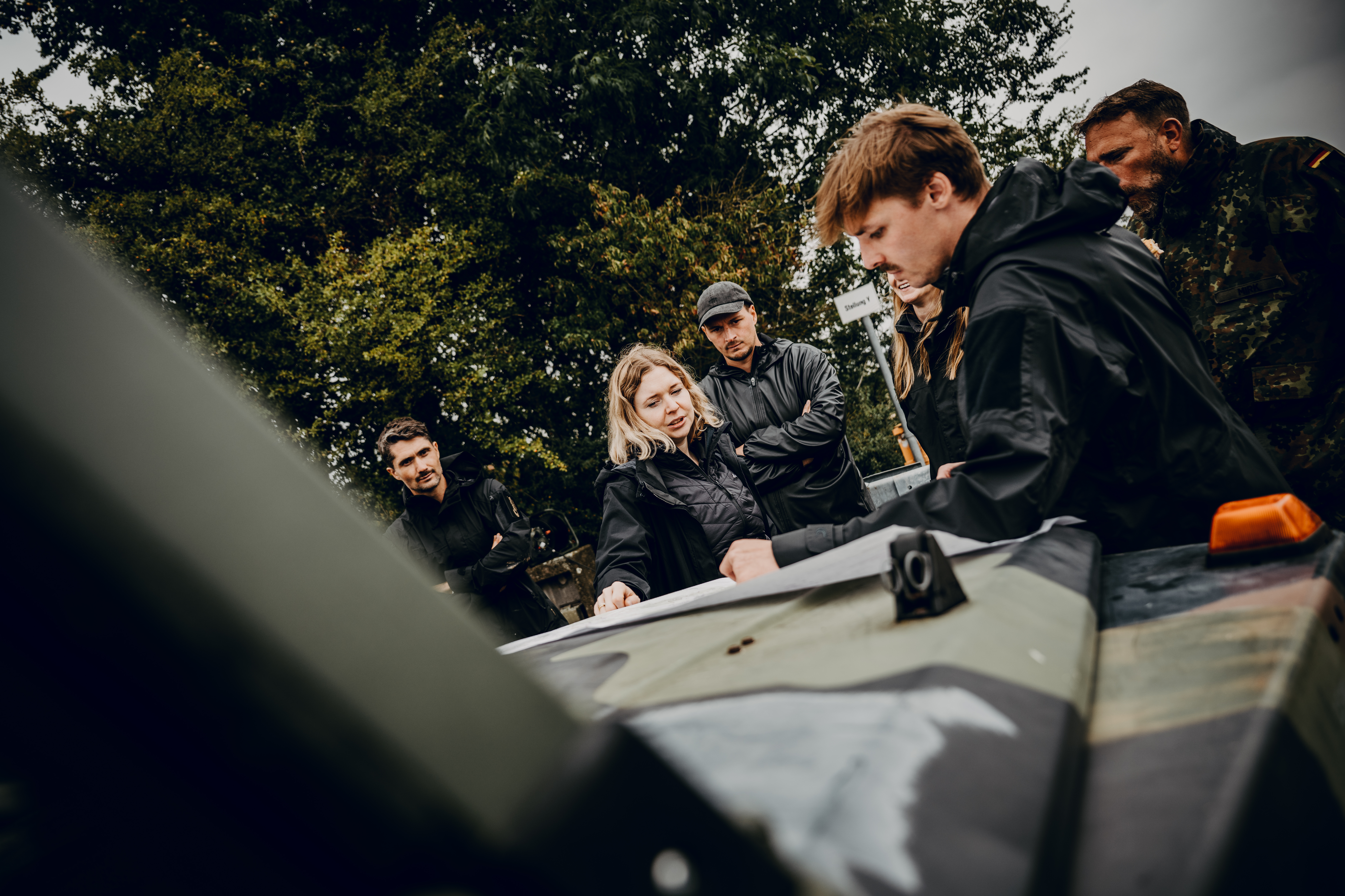 Eine Gruppe Soldaten und Zivilisten stehen um die Motorhaube eines Bundeswehr Jeeps und schauen auf eine Karte.
