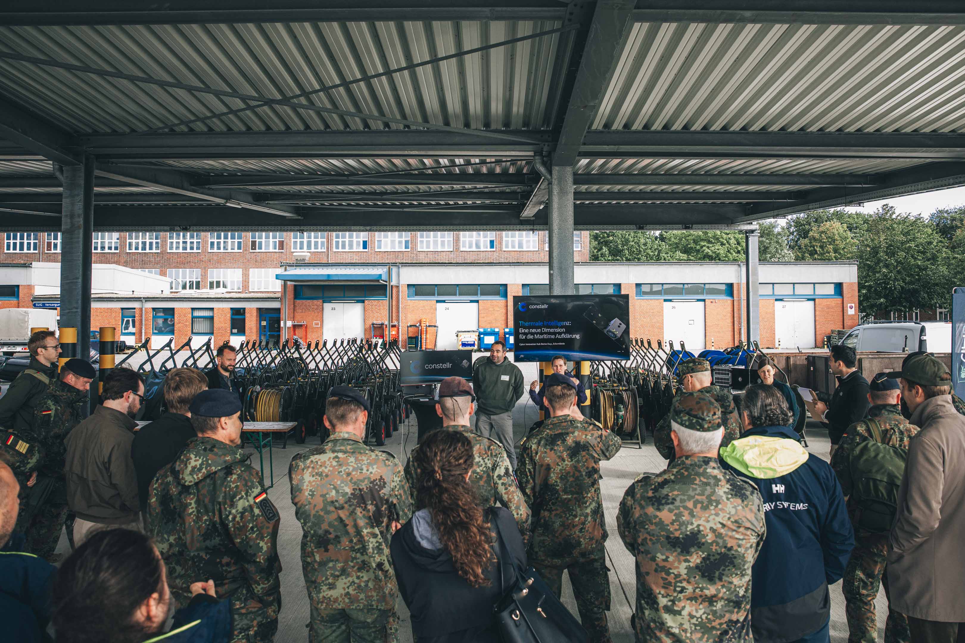 Ein Zivilist erklärt unter einem Schleppdach einer Gruppe Soldaten sein Produkt.