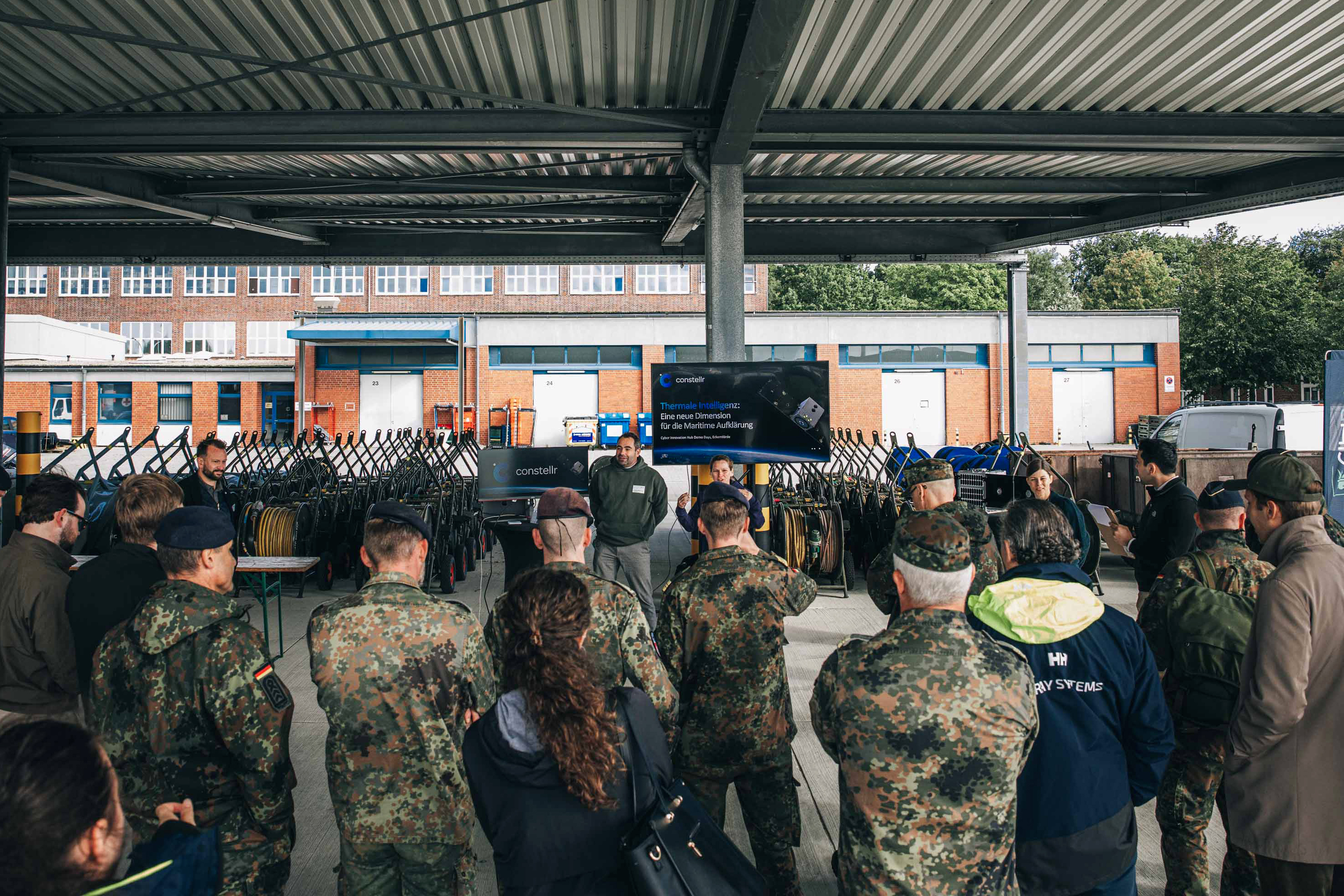 Ein Zivilist erklärt unter einem Schleppdach einer Gruppe Soldaten sein Produkt.
