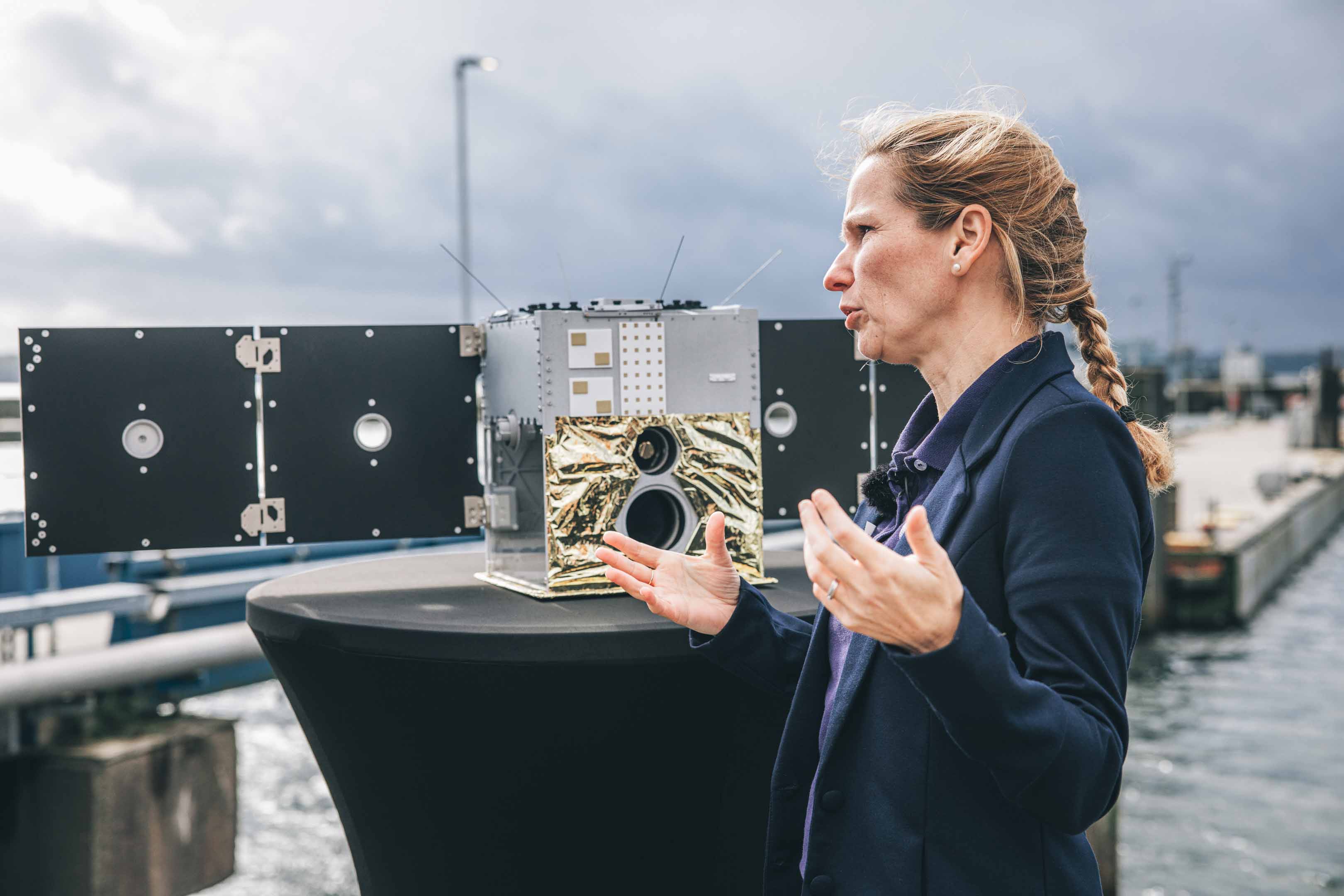 Eine Frau steht mit den Händen gestikulierend an einem Stehtisch, auf dem eine technische Apparatur steht.
