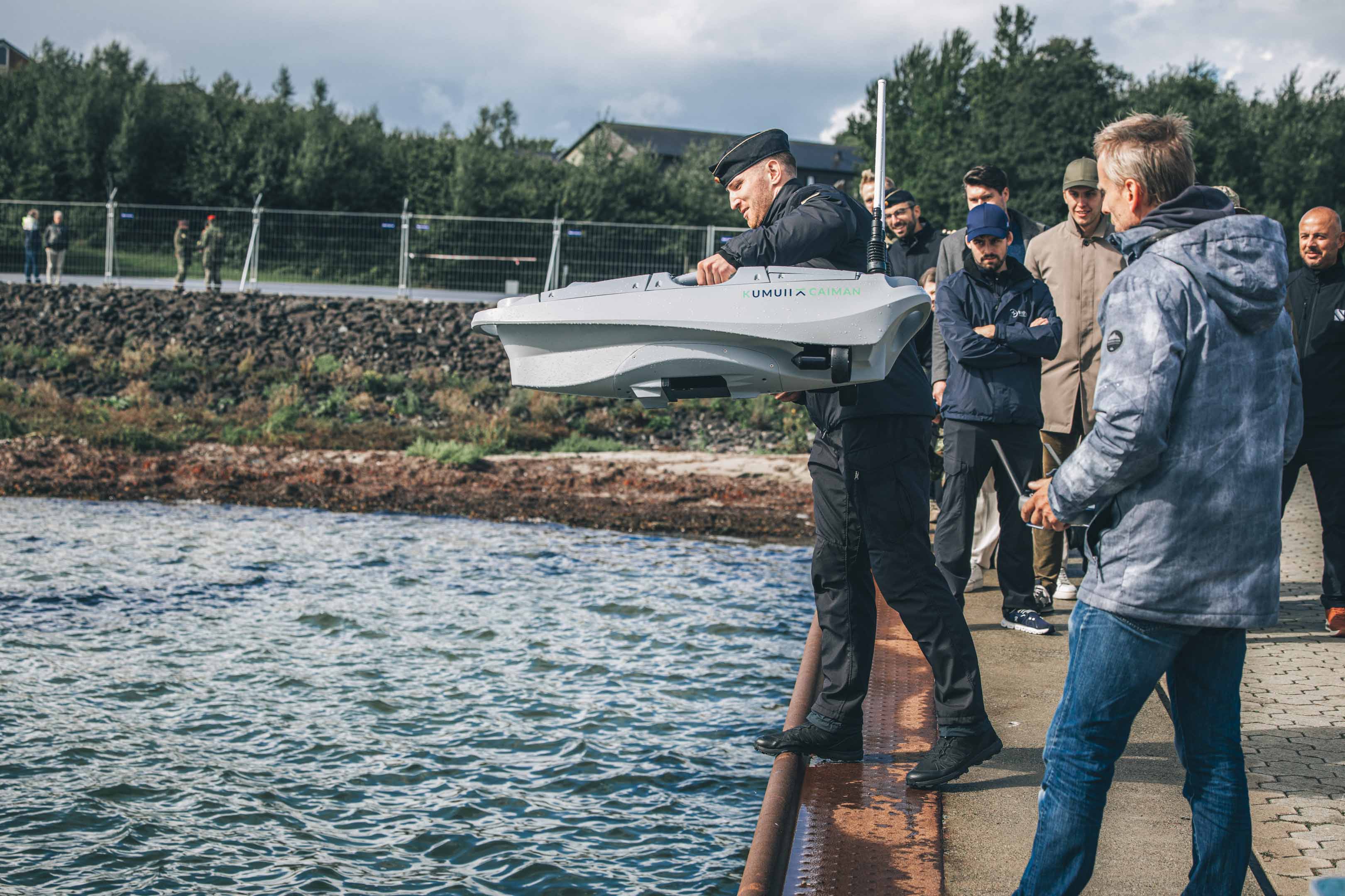 Eine Marine Soldat lässt an der Kaimauer den Prototypen eines unbemannten Bootes zu Wasser. Neben ihm steht ein Vertreter des Startups.
