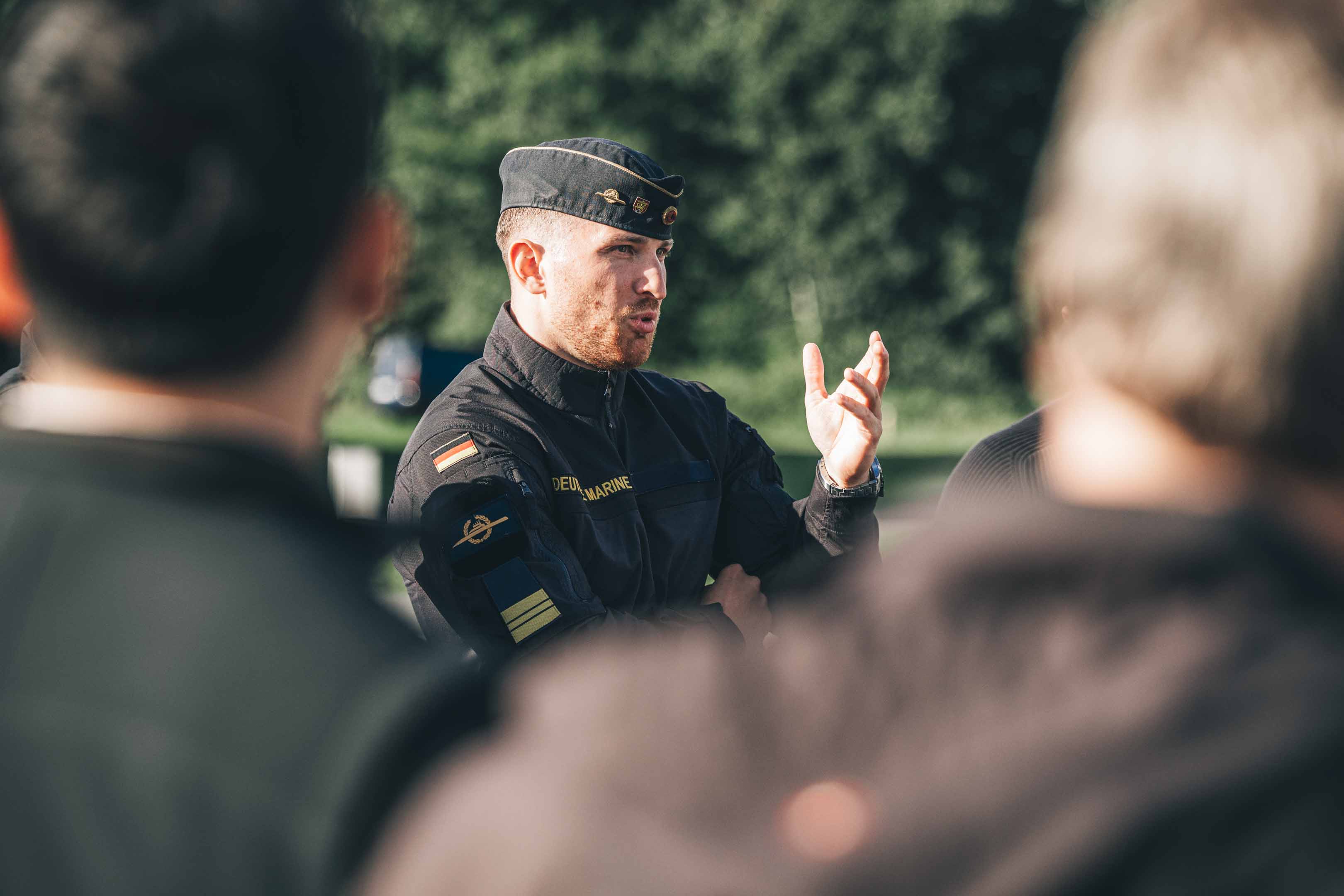 ein Marinesoldat spricht zu einer Gruppe Zivilisten, die von hinten zu sehen sind.