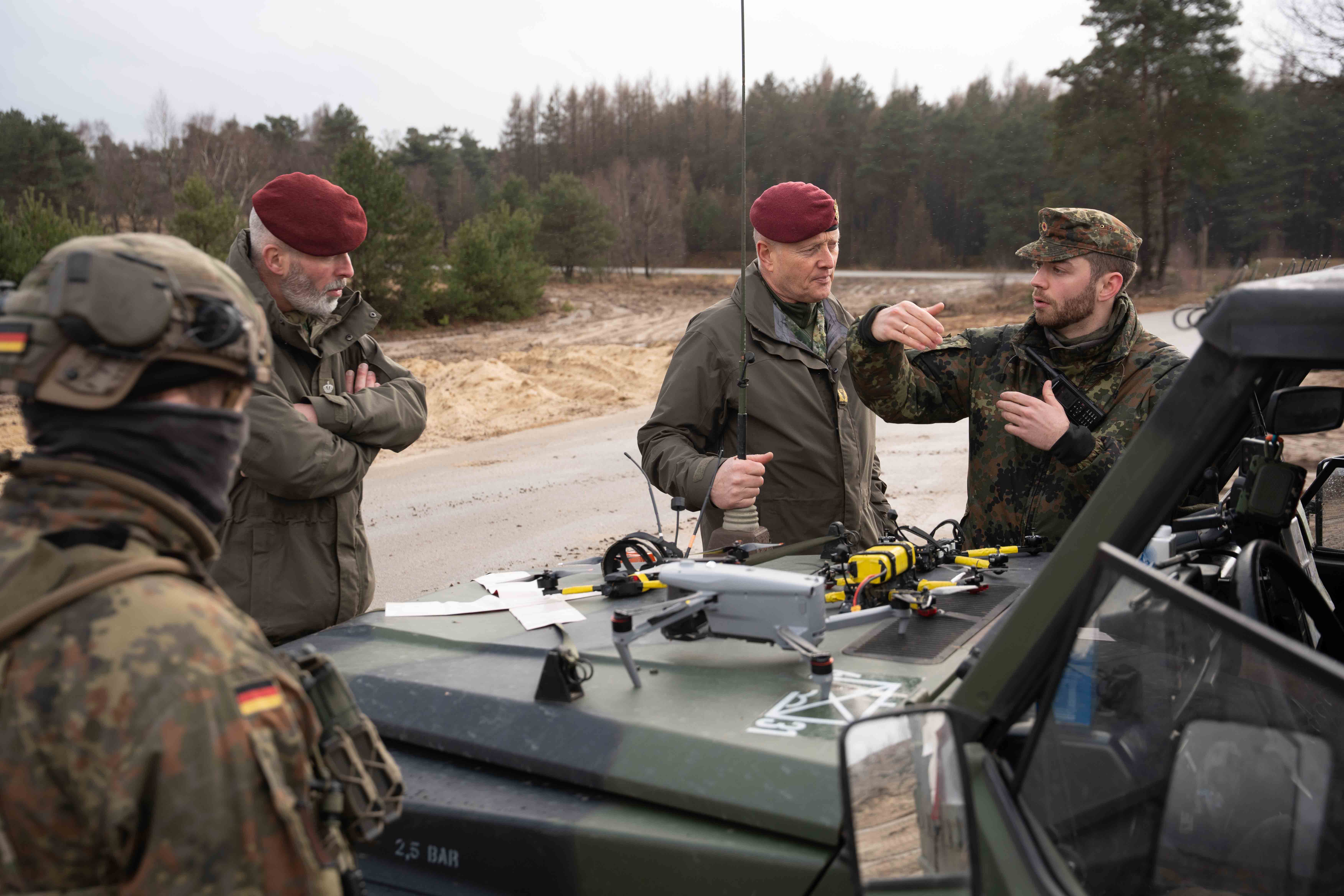 Eine Gruppe Soldaten steht an der Motorhaube eines Bundeswehr-Jeeps, auf der eine Drohne liegt.