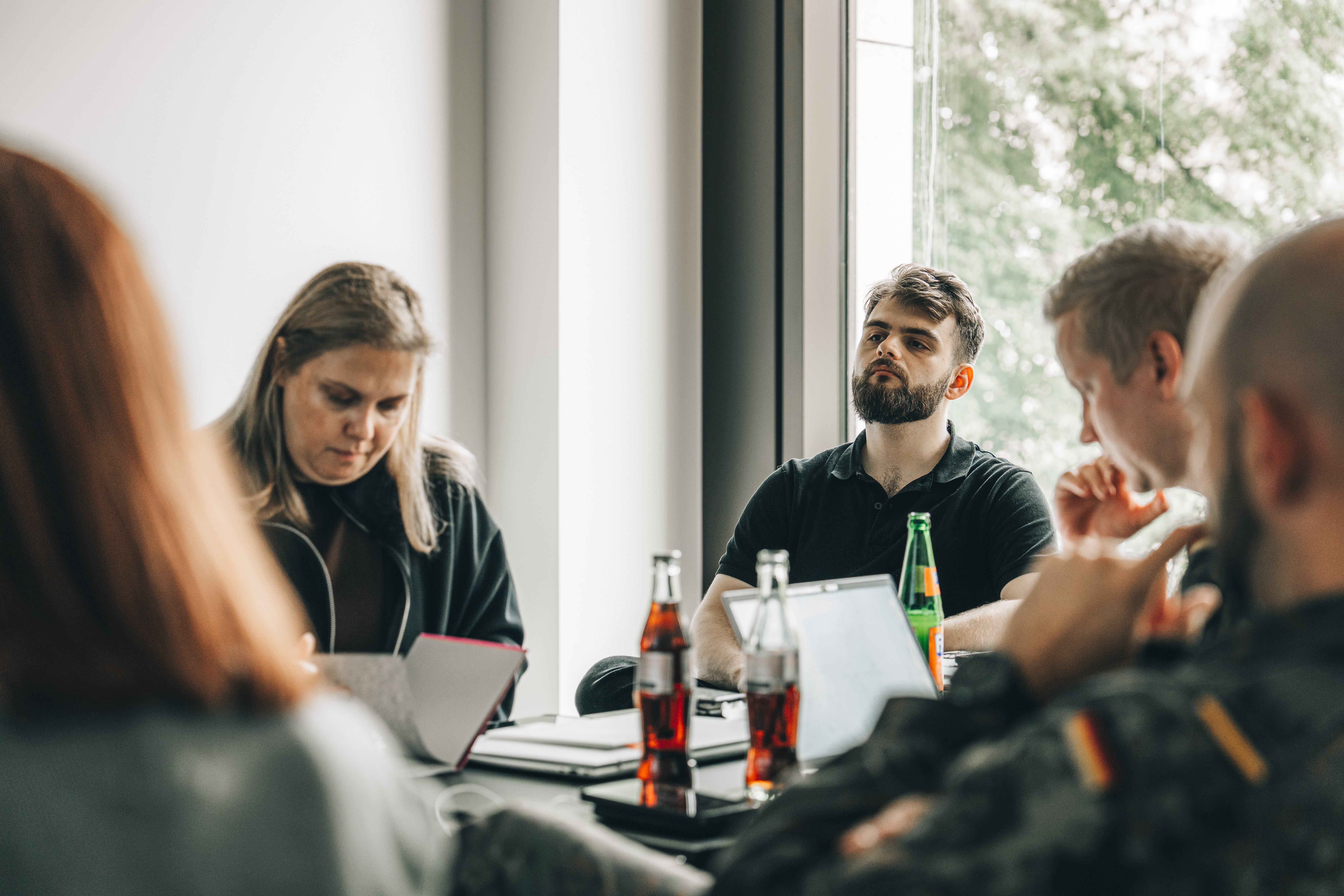 In einem Besprechungsraum sitzen Zivilisten und Militärs um einen Tisch und arbeiten gemeinsam an Laptops.