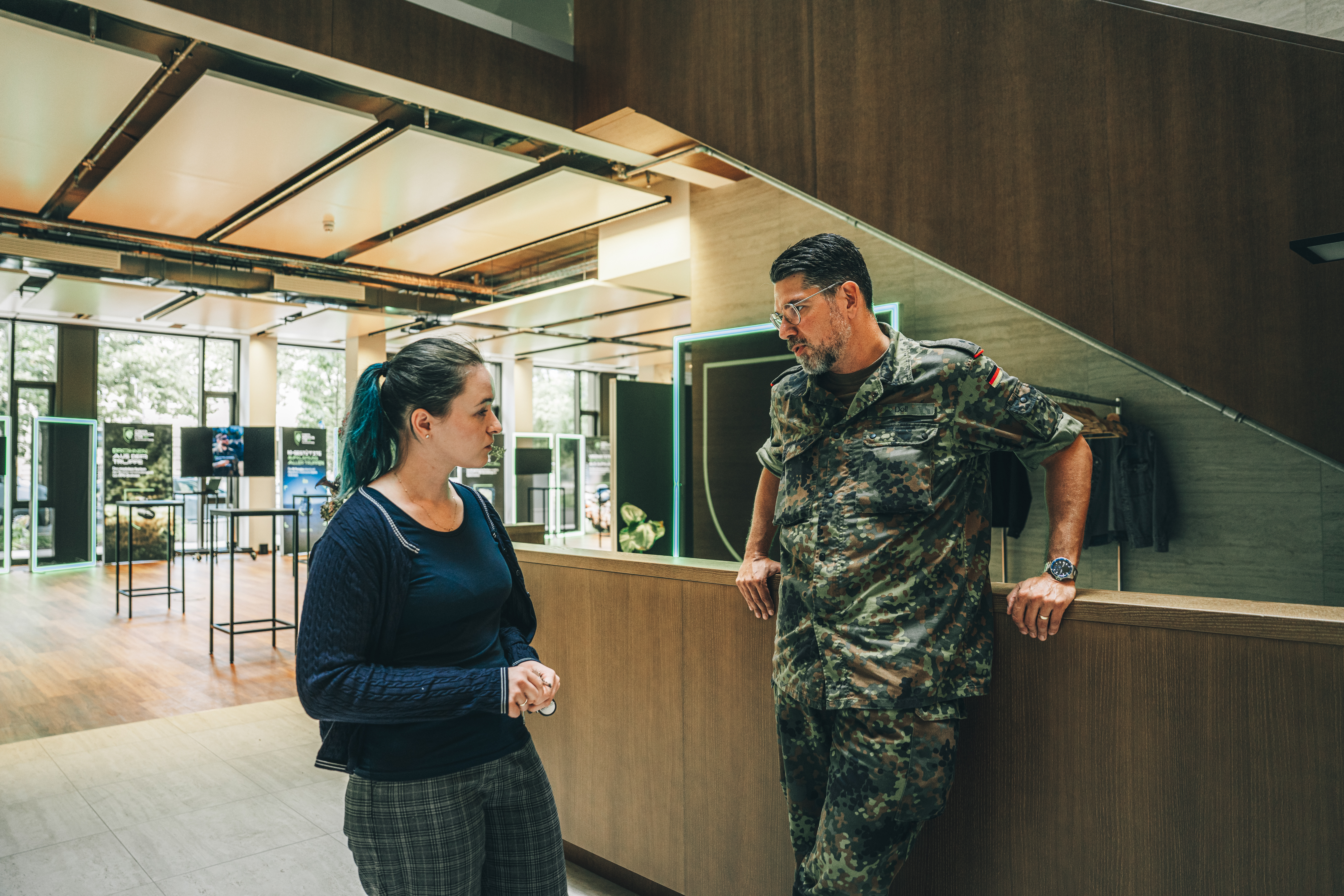 Ein Soldat steht angelehnt an einem Empfangstresen und unterhält sich angeregt mit einer Zivilistin. Im Hintergrund ist die Eventfläche des Schöneberger Ufers zu sehen.